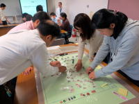 住民が一次避難所での生活を模擬し、問題解決に取り組む様子。テーブルには多くの資料や道具が広がっている。