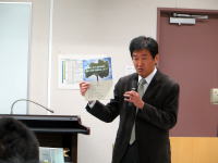 除染・里山再生活動について説明する男性が資料を持っている様子。