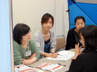 医療に関する話し合いをしている女性たちのグループ。テーブルには資料が置かれ、真剣な表情で意見を交わしている。