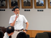 福島県立医科大学の講演会で話す男性、背景には歴代の学長の肖像画が飾られている。