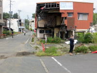 福島県の街角にある、崩れた建物と人々が写る風景。
