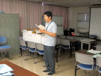 被ばく汚染傷病者受入実習の手順を説明する男性が教室で資料を読み上げている様子。