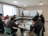 会議室で資料を前にして議論する参加者たちの様子。講師が説明を行っている。