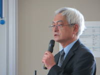 福島県立医科大学の院長が講演中の様子。マイクを持ち、真剣な表情で話している。