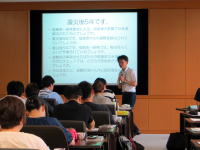 講義を行う講師と受講生が座っている教室の様子。スクリーンにはプレゼンテーションが表示されている。