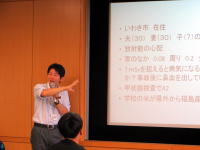 プレゼンテーション中の講師がスライドを指し示している様子。背景には情報が表示されたスクリーンがある。