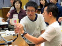 医療に関する研修中の参加者が、実習用の器具を使っている様子。背景には他の参加者が見える。