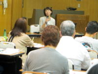 講演を行う女性と聴衆が座っている会場の様子。