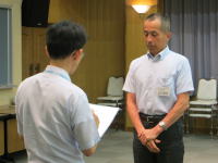 医療に関する会議で話を聞く男性とメモを取る男性の様子。