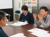 福島県立医科大学での会議中の様子。3人の男性がテーブルを囲み、意見を交わしている。