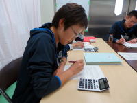 学生が机に向かい、計算機を使いながらノートに書き込んでいる様子。