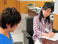 医療現場で患者と向き合う女性医師が、メモを取りながら話を聞いている様子。