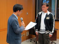 福島県立医科大学の授与式で、スピーチをする男性と受賞者が立っている様子。