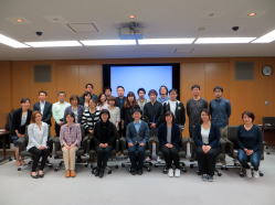 福島県立医科大学の会議室でのグループ写真、参加者が椅子に座り、前方のスクリーンを背景にしている。