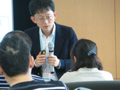 福島県立医科大学での講演中の男性がマイクを持ち、聴衆に向けて話している様子。
