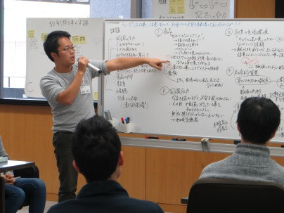 医療関係者向けのリスクコミュニケーションについて説明する講師と受講者の様子。ホワイトボードには多くのメモが書かれている。