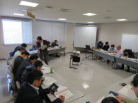 会議室で参加者が資料を読みながら討論している様子。机にはノートやタブレットが置かれ、真剣な雰囲気が漂う。