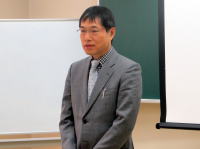 福島県立医科大学で講演を行う男性がスーツ姿で立っている様子。背景にはホワイトボードが見える。
