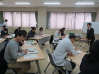教室で講義を受ける学生たちが、ノートにメモを取りながら真剣に学んでいる様子。
