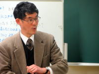 福島県立医科大学で講義を行う男性の教授が、黒板の前で話している様子。