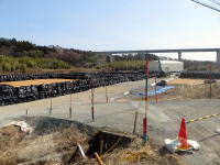 福島県立医科大学近くの工事現場の風景。黒い資材が整然と並び、遠くには高架橋が見える。