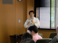 医療に関する講演を行う白衣を着た男性と、聴衆がいる会場の様子。