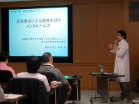 医師がプレゼンテーションを行っている様子。背景にはスライドが映し出されている。