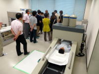 医療機器の前で説明を受ける人々と、機器に横たわる患者の様子。福島県立医科大学の医療現場を示す。