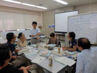 福島県立医科大学の教室で、講師が参加者に説明を行い、グループディスカッションをしている様子。