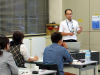講義中の男性がプレゼンテーションを行い、参加者が聴講している様子。