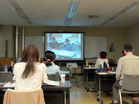 教室で講義を受ける学生たちが、スクリーンに映し出された内容を見つめている様子。