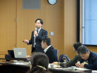 福島県立医科大学での健康管理調査に関するプレゼンテーションの様子。講演者がマイクを持ち、参加者が聴講している。