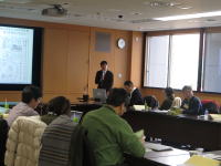 会議室でプレゼンテーションを行う講師と参加者たちの様子。