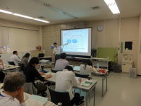福島県立医科大学の教室で、講師がスライドを指し示しながら説明している様子。受講者が座って聴講している。