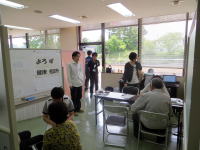 飯舘村の健康相談会の様子。参加者がテーブルに座り、医療スタッフと対話している。窓からは自然光が差し込む明るい室内。
