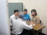 健康相談を受ける人々がテーブルを囲んで話し合っている様子。医療従事者と相談者が対話を重ねている。