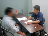 健康相談を行う医療従事者と相談者が対面している様子。テーブル上には書類が置かれている。