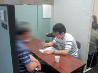 健康相談を受ける男性と、メモを取る医療従事者が写る相談室の様子。