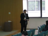 第44回医学教育セミナーで司会を務める石川和信氏が講演を行っている様子。背景には窓と観客席が見える。