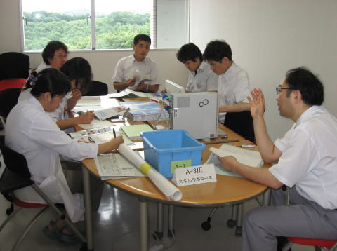医療教育に関する会議を行う福島県立医科大学の学生たち。テーブルには資料やパソコンが置かれ、真剣な表情で議論している様子。