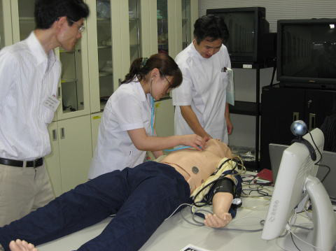 医療シミュレーターを使っている学生たちが、実習中に人形の胸部に機器を取り付けている様子。