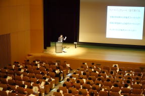 全員参加型のFD講習会で講演を行う講師と、聴衆が座る様子。
