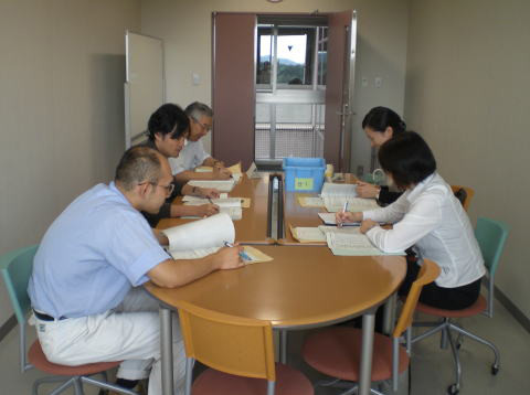 会議室で資料を持ちながら話し合う5人の人々の様子。