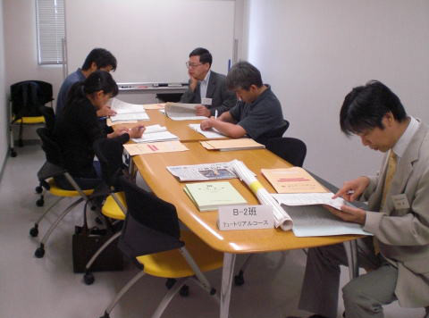 テーブルを囲んで資料を読み込む5人の参加者がいる会議の様子。