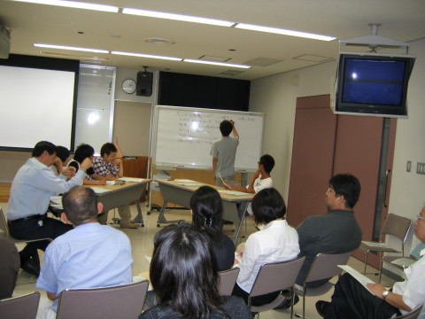学生が模擬テュートリアルを行っている教室の様子。ホワイトボードに向かう学生と、座っている参加者たちが見える。
