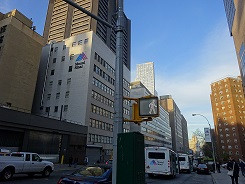 都市の街並みが広がる風景で、ビルが立ち並ぶ通りの様子を捉えた画像。信号機には歩行者用の表示が見える。