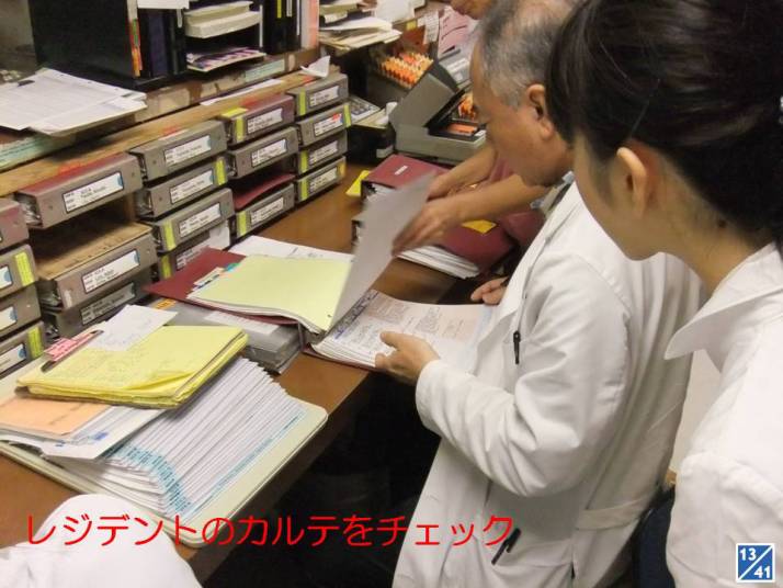 医療スタッフが書類を確認している様子、デスク上には多くのファイルやカルテが散らばっている。