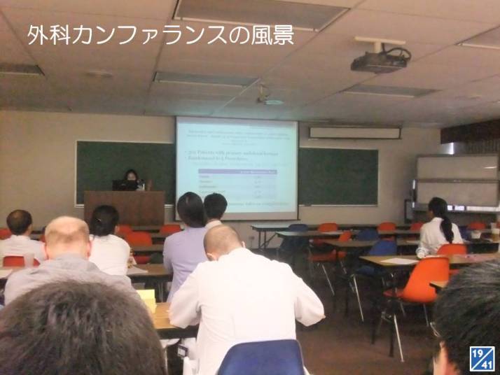 外科カンファレンスの風景。講演者がプレゼンテーションを行い、参加者が聴講している様子。
