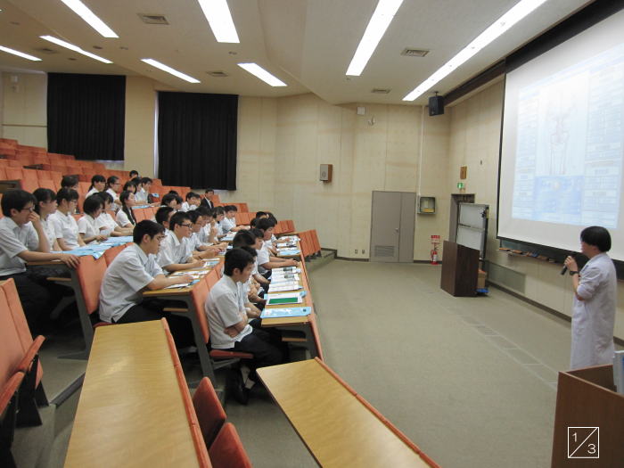 福島成蹊中学校の教室で、講師が生徒に向けてプレゼンテーションを行っている様子。生徒たちは熱心にメモを取っている。
