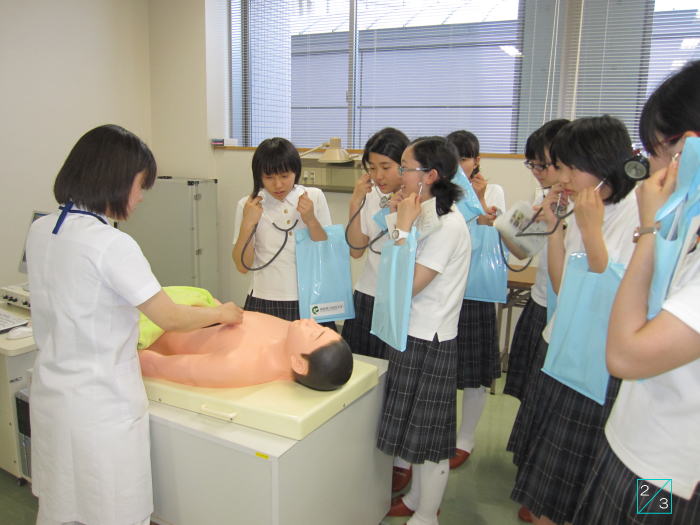 福島成蹊中学校の見学中、医療実習を受ける生徒たちが人形に聴診器を当てている様子。